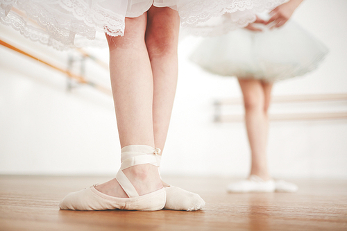 Legs of little girl wearing satin points and shiffon skirt during ballet lesson