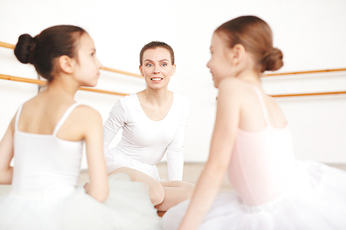 Young ballet teacher looking at one of her talking learners after lesson