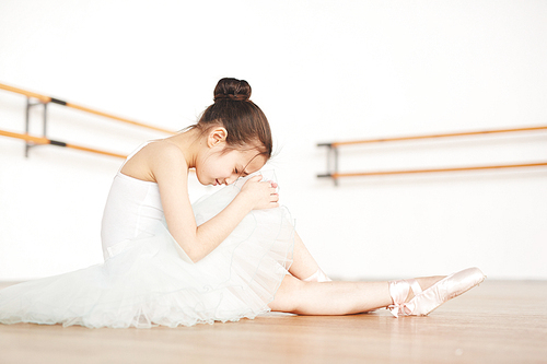 Cute girl in ballerina outfit sitting on the floor of classroom and crying because of dancing troubles