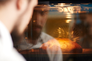 Chef looking at hot bread in oven