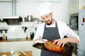 Pastry-baker touching crusty loaf of bread on tray