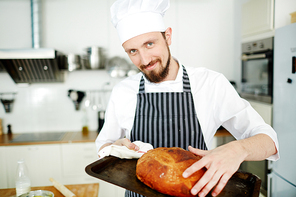 Young pastry baker taking hot loaf of bread off tray