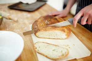 Baker cutting loaf of crusty bread on wooden board