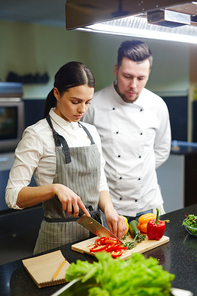 Young woman curtting pepper with chief near by