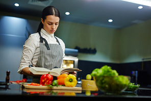 Young woman with cookery book preparing food at home