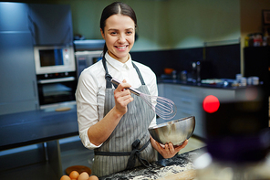 Young woman whisking raw eggs in mixing-bowl in front of camera