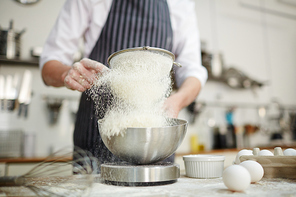 Baker sifting wheaten flour into bowl while preparing dough