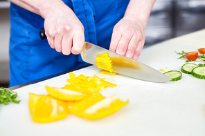 Hands of trainee cutting fresh pepper and other vegs on table