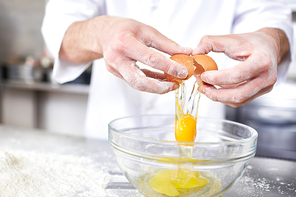 Chef breaking raw egg into bowl while preparing dough