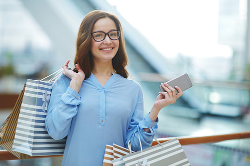 Happy young woman with smartphone and paperbags