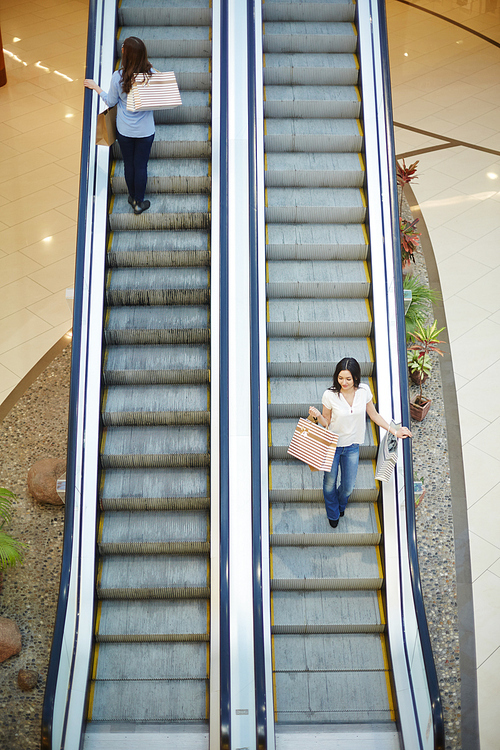 Young shoppers moving up and down on escalator