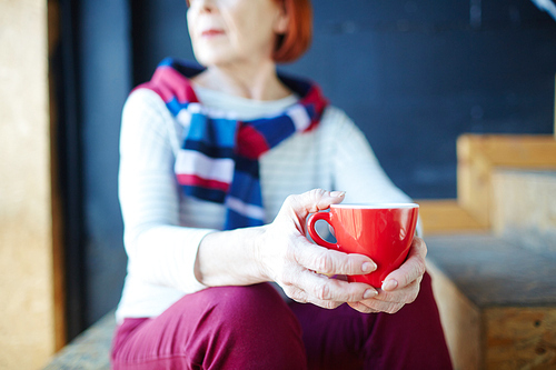 Red mug with hot drink in hands of relaxed senior woman