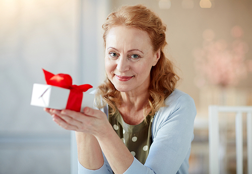 Portrait of elegant mature woman  and smiling holding gift box in home interior