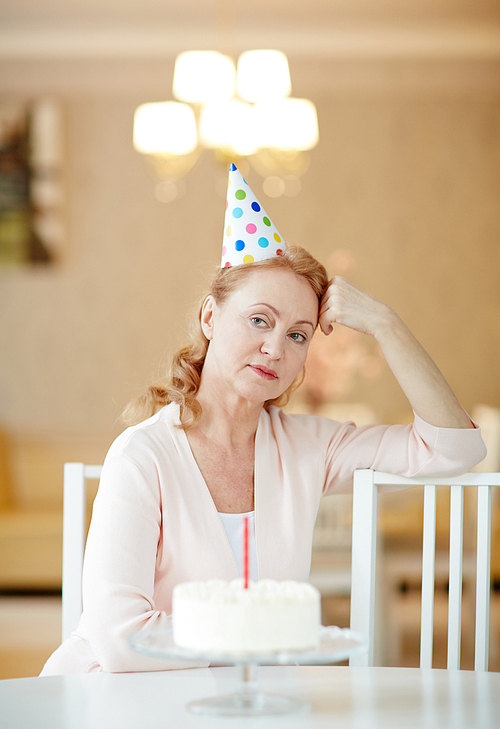 Offended female in birthday cap sitting on chair by table