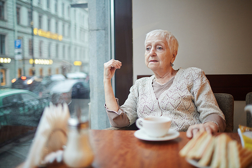 Retired woman having rest in one of city cafeterias