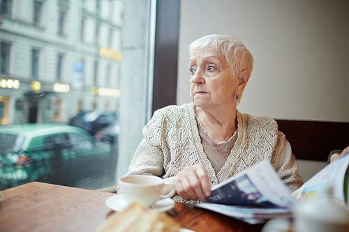 Tense woman with journal looking through window while sitting in cafe