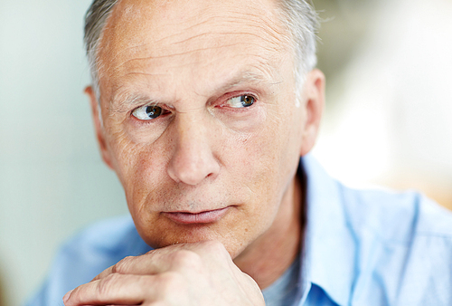 Headshot of handsome senior man wearing blue shirt looking away pensively, blurred background