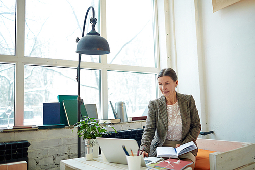 Senior financial manager wrapped up in work: she sitting in cozy small cafe with panoramic windows and preparing annual accounts on laptop, waist-up portrait