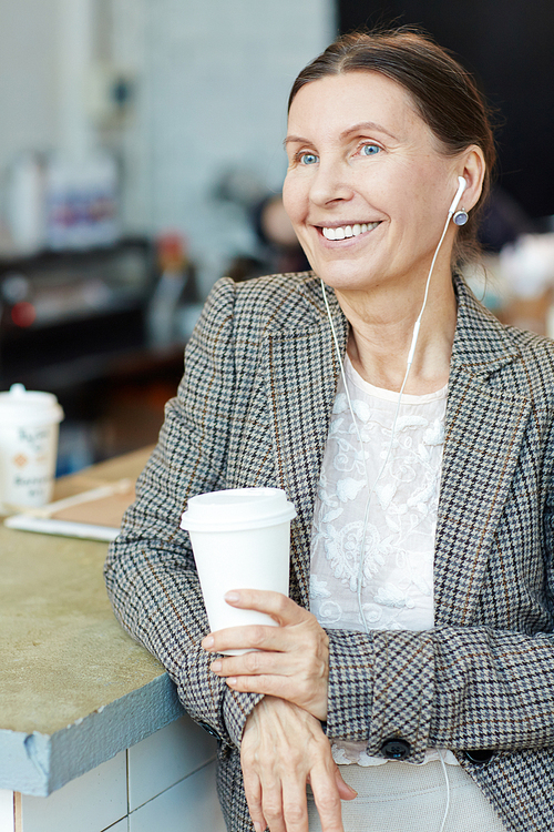 Happy mature woman with earphones having coffee break