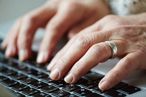 Hands of senior woman pressing buttons on laptop keyboard, close-up shot