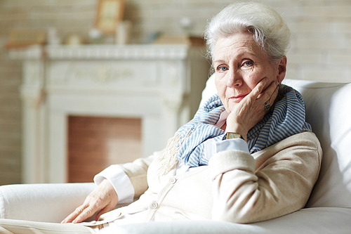 Pretty elderly woman in white shirt and beige cardigan leaning on elbow and  with slight smile