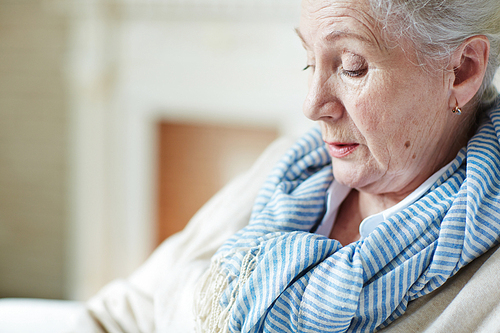 Close-up view of elegant old woman in blue-and-white striped scarf sitting and looking down pensively