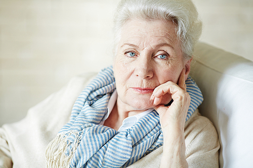 Portrait of elegant blue-eyed elderly woman in beige cardigan and striped scarf looking away thoughtfully
