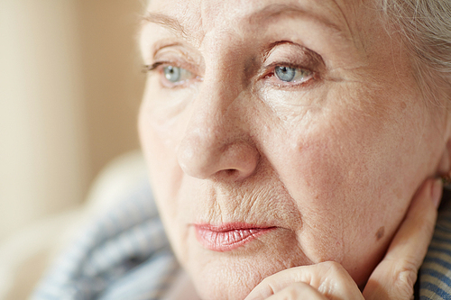 Extreme close-up shot of wrinkled retired woman with light make-up looking away pensively