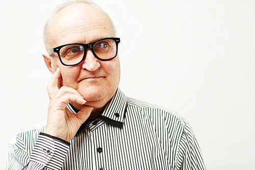 Headshot of pensive male senior in eyeglasses and elegant striped shirt propping his head with hand and looking to the side