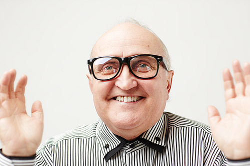 Portrait of funny old gentleman in eyeglasses and striped shirt smiling happily with teeth while standing in pose of catching a ball