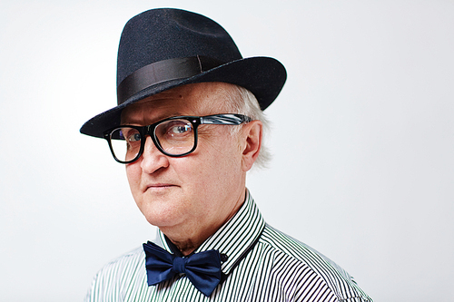 Headshot of stylish senior man in black hat and striped shirt with bowtie  disapprovingly isolated on white