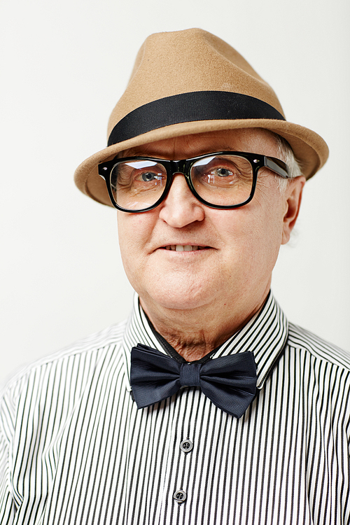 Portrait of good-looking old gentleman in hat, eyeglasses and striped shirt with bow tie  and smiling on white background