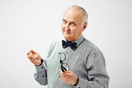 Portrait of confident bald senior man in striped shirt with bow tie holding eyeglasses,  with quizzical smile