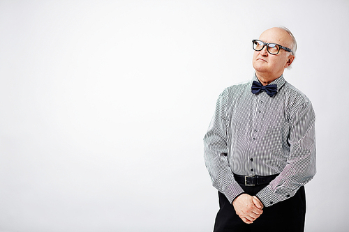 Portrait of stylish elderly man standing with his hands clasped and looking upwards pensively against white background