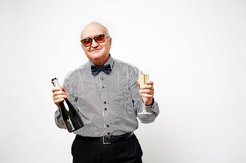 Portrait of dressed-up senior man in sunglasses holding champagne bottle and smiling brightly isolated on white