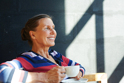 Happy retired female with cup of tea relaxing in cafe