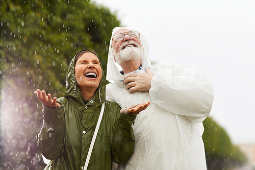 Ecstatic female and her husband in raincoats enjoying rainy weather in natural environment