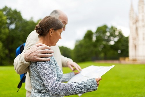 Senior husband embracing his wife by shoulder and pointing at map guide in her hands during trip