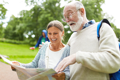 Aged man pointing at map during discussion of destination place with his wife