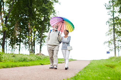 Couple of pensioners talking while going down country road under colorful umbrella