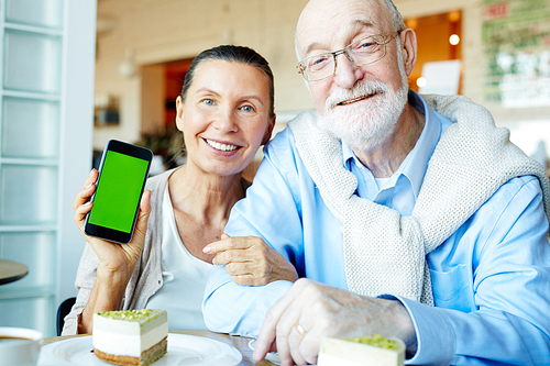 Smiley senior couple with gadget relaxing in cafeteria
