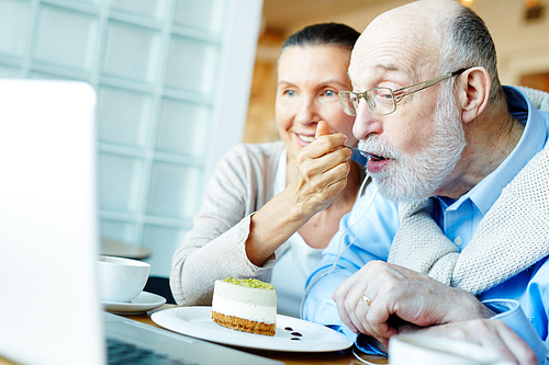 Senior woman feeding her husband while he networking