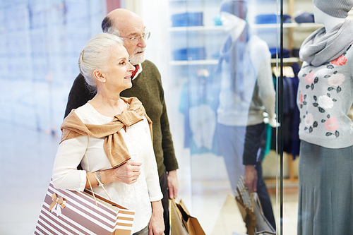 Senior couple with paperbags looking at clothes in display-window
