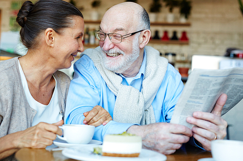 Senior man with newspaper and his wife talking by dessert in cafe