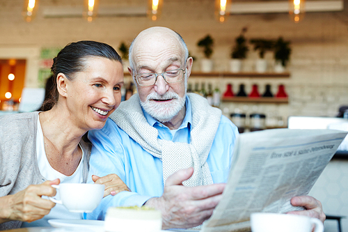 Mature man showing his wife latest news by cup of tea