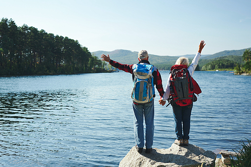 Adventurous seniors waving hands in front of lake