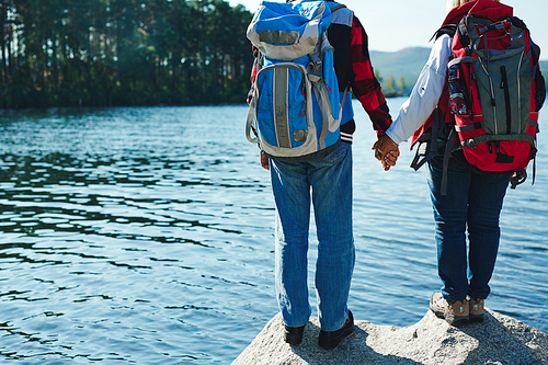 Seniors with backpacks holding by hands while standing on big stone