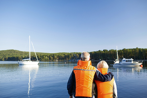 Affectionate seniors in protective vests looking at yacht in the lake