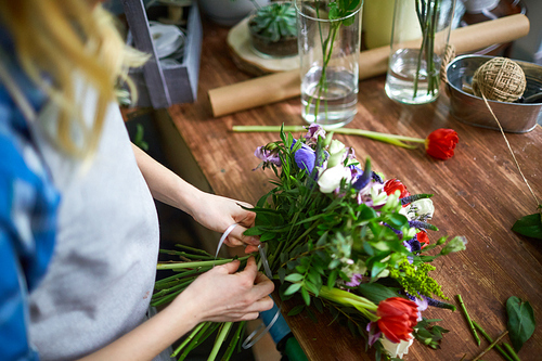 Female florist arranging bouquet and tying it with thin ribbon