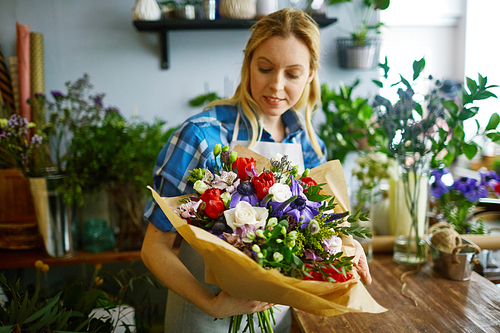 Young florist looking at arranged bouquet in her hands